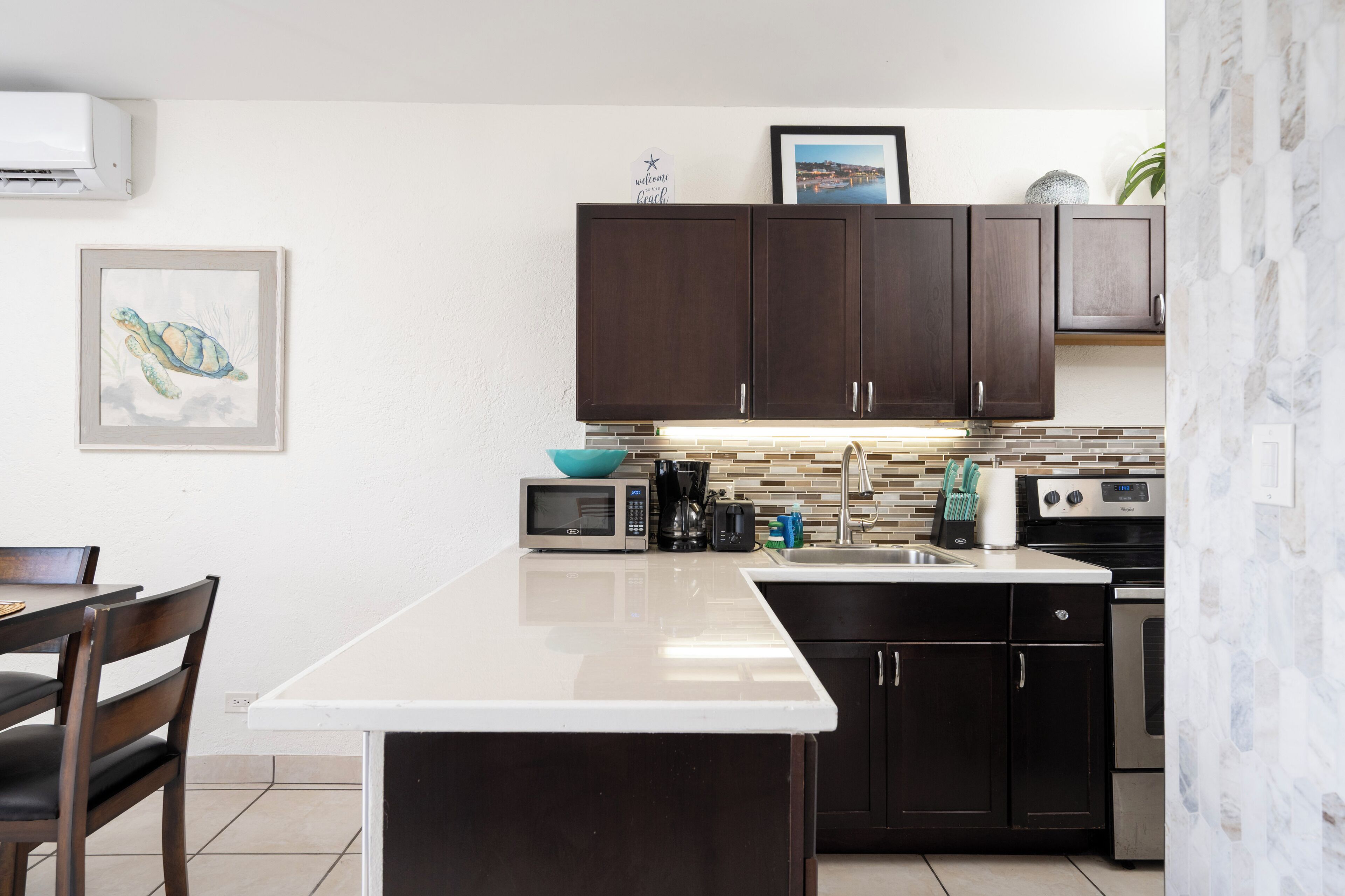 A kitchen with dark wooden cabinets, a white countertop, a microwave, a toaster, and a sink.