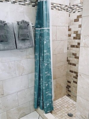 Un espace douche avec un rideau de douche de couleur turquoise, des murs carrelés et un banc où sont posées des serviettes.