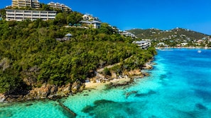 Una zona costera con un mar turquesa transparente, una playa de arena y una colina con edificios.