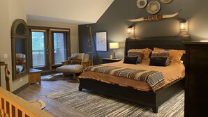 Ein Schlafzimmer mit einem dunkelbraunen Bett, einem Holz-Kopfteil und einem großen Fenster mit Jalousien.