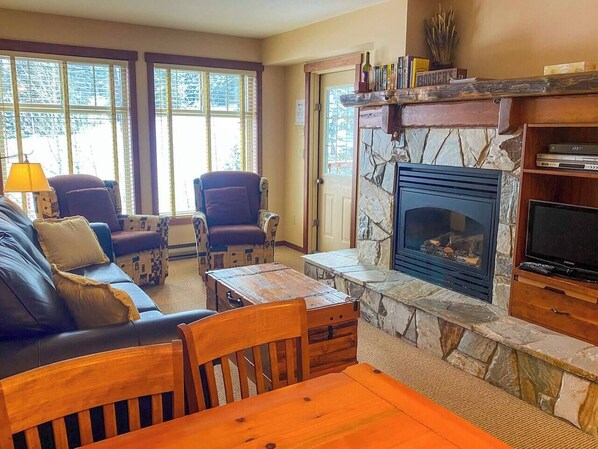 A cozy living room with a fireplace, leather sofa, wooden coffee table, and two armchairs.
