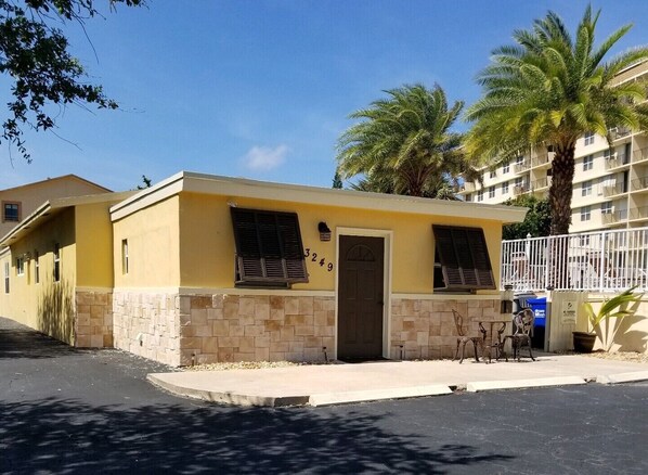 Un bâtiment jaune avec un rez-de-chaussée en pierre, une porte et deux fenêtres dotées de volets.