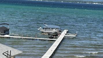 Un muelle se adentra en una masa de agua tranquila, con barcos amarrados, un cielo despejado y una costa distante con edificios.