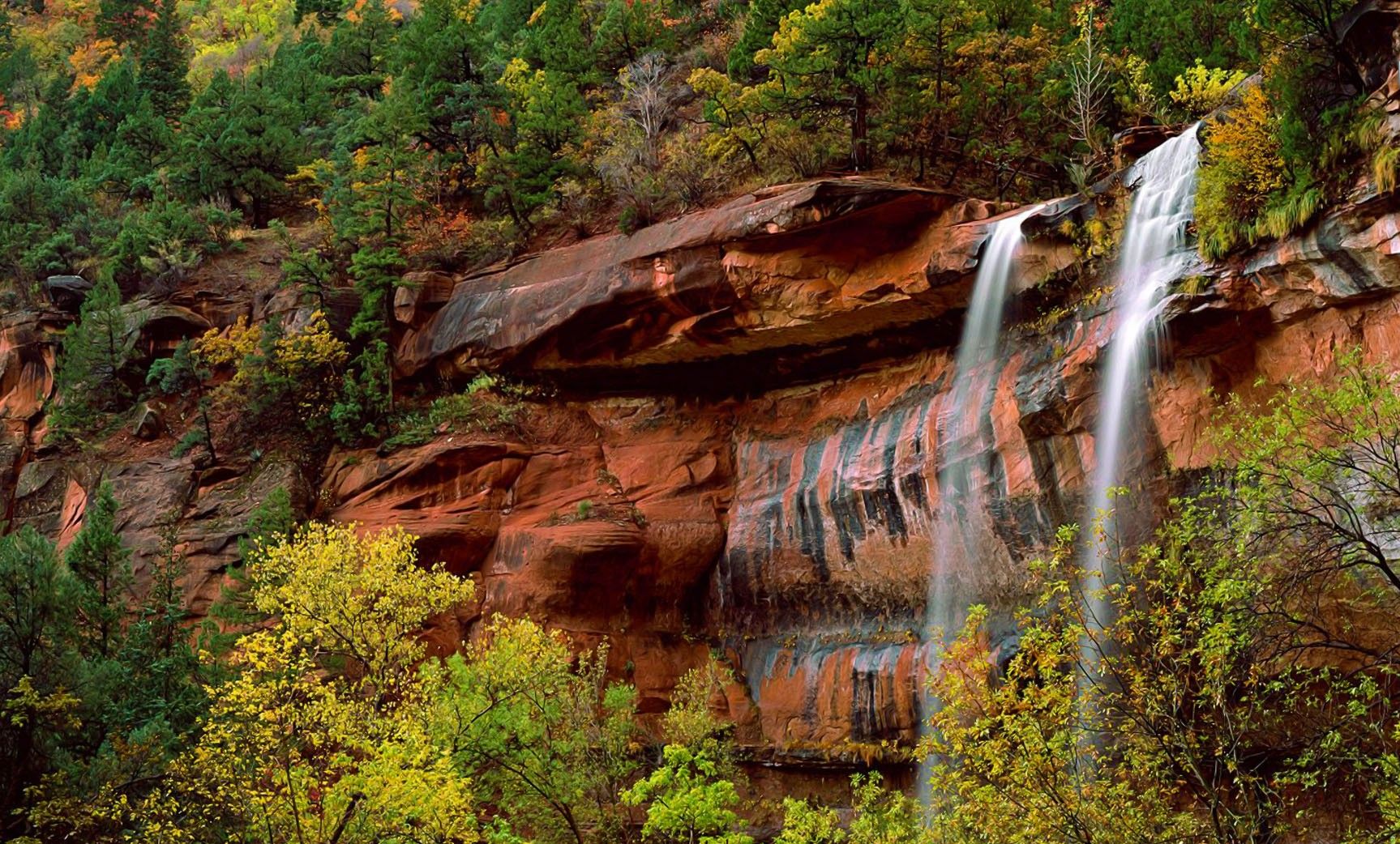 Une cascade se déversant le long d’une falaise rocheuse, entourée d’une végétation luxuriante.