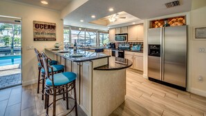 A modern kitchen with a central island, bar stools, stainless steel appliances, and a view of the outdoors.