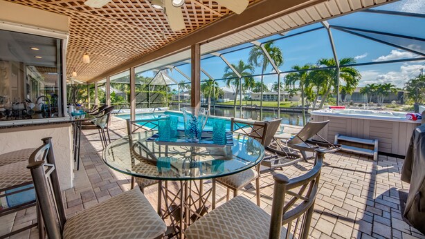 An outdoor patio with a glass table, chairs, and a hot tub.