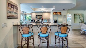 A modern kitchen with a central island, bar stools, and a decorative wall sign.