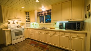 A kitchen with white cabinets, a stove, a microwave, and a coffee maker. - Quiet and Peaceful 3 Bedroom Family Cottage on Lake George, 12 Miles to TC (Traverse City)