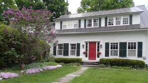 Una casa de dos pisos con puerta frontal roja, revestimiento blanco y contraventanas verdes.