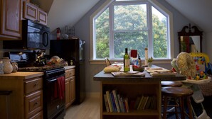 Una cocina con armarios de madera, una estufa negra y un amplio ventanal con vista a árboles.