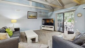 A living room with a TV, sofa, and a small table. There is a sliding glass door leading to an outdoor area. - Inviting Palmetto Dunes condo w/ pool, private W/D & deck near beach & golf (Hilton Head Island)