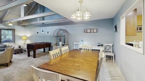 A spacious room with a large wooden dining table, white chairs, a foosball table, and a chandelier. - Inviting Palmetto Dunes condo w/ pool, private W/D & deck near beach & golf (Hilton Head Island)