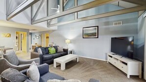 A modern living room with a high ceiling, a flat-screen TV, and a sofa. - Inviting Palmetto Dunes condo w/ pool, private W/D & deck near beach & golf (Hilton Head Island)