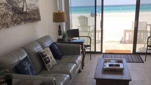Ein Wohnzimmer mit einer Ledersofa, einem Holztisch und Blick auf den Strand durch große Glasfenster.