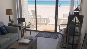 Ein Wohnzimmer mit Blick auf den Strand, einem Deckenventilator und einem Tisch mit Lampe.