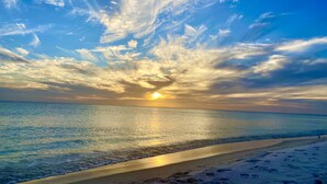 Ein Strand mit blauem Himmel und der Sonne, die am Horizont untergeht oder aufgeht.