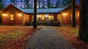 A two-story log cabin with a stone foundation, a front porch, and a gravel driveway.