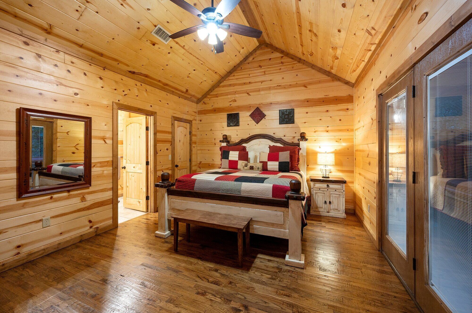 A wooden cabin bedroom with a bed, a nightstand, a mirror, and a ceiling fan.
