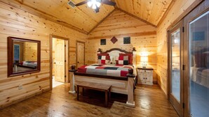 A wooden cabin bedroom with a bed, a nightstand, a mirror, and a ceiling fan.