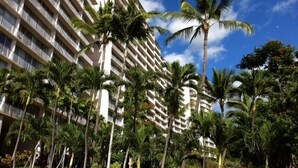 A high-rise hotel with multiple balconies, surrounded by palm trees and lush greenery.