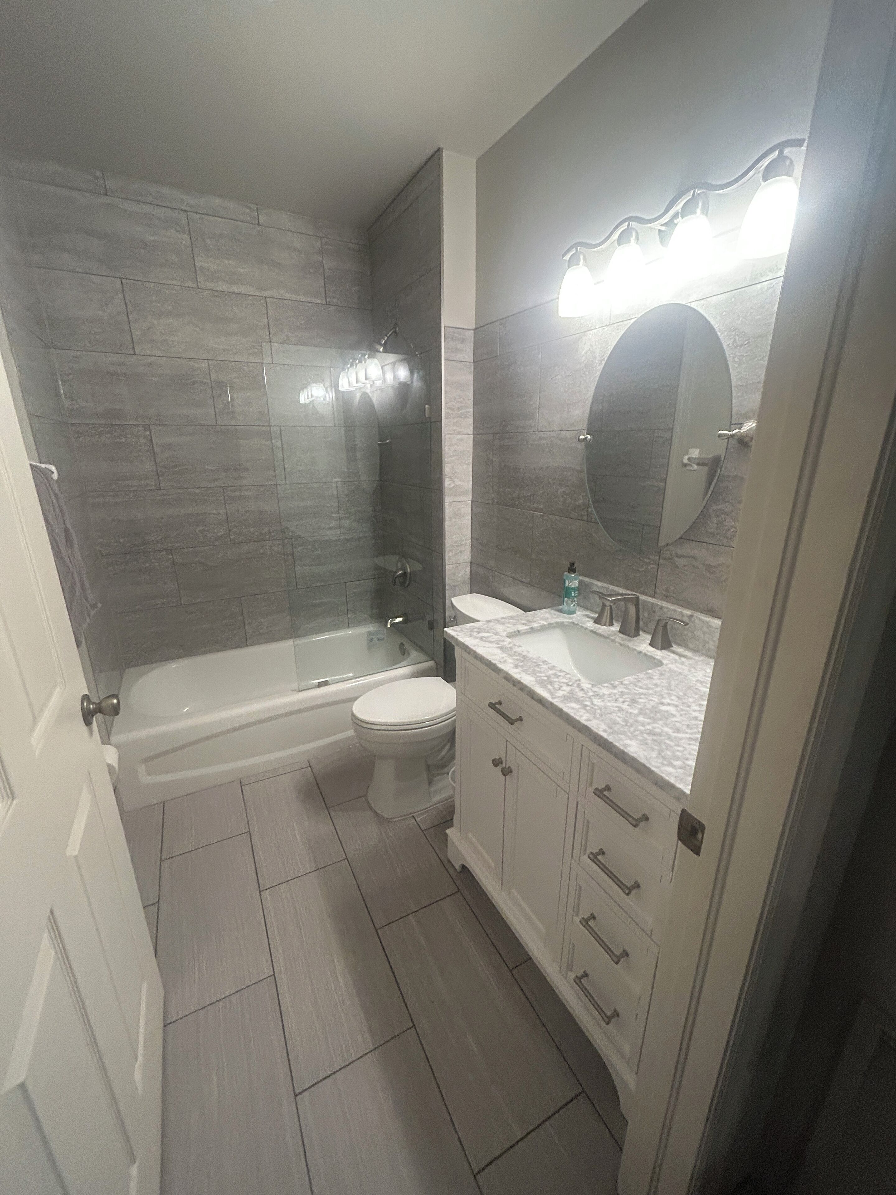 A bathroom with a bathtub, toilet, vanity, and a large mirror.