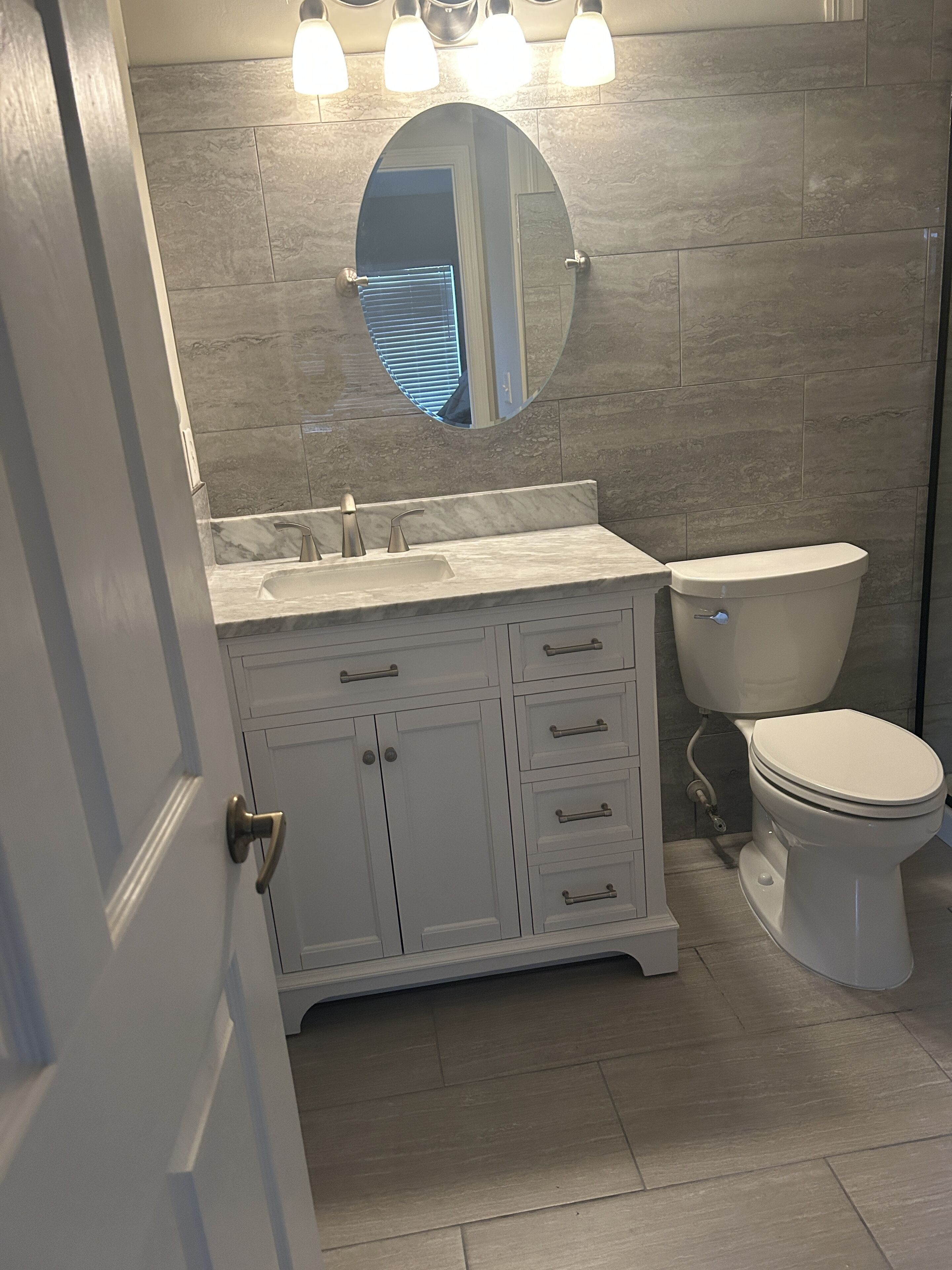 Une salle de bain avec un meuble-lavabo blanc, un miroir rond, des toilettes et un luminaire placé au-dessus du miroir.