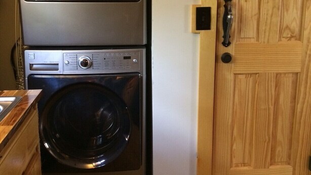A stacked washer and dryer unit in a laundry room with a wooden door.