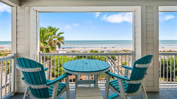 Een balkon met uitzicht op het strand, twee stoelen en een tafel.