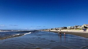 Een strand met heldere lucht, golven en mensen die wandelen.