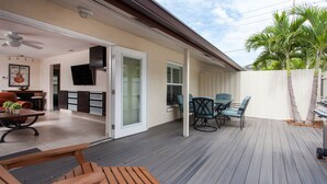 Un patio techado con mobiliario de madera, un televisor montado en la pared y una palmera.