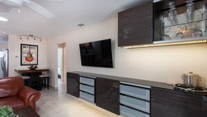 Una cocina moderna con encimera oscura, televisor de pantalla plana y vitrina de vidrio con copas de vino.