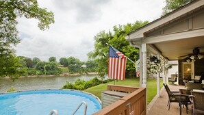A swimming pool with a wooden deck, an American flag, and a covered patio area with outdoor furniture. - Riverfront, Kayaks, Boat Dock, Games, Pool, Hot Tub, 10 Min To Dwntwn Nashville! (Nashville)