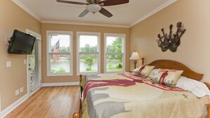 A bedroom with a bed, a ceiling fan, a mounted television, and windows with an American flag. - Riverfront, Kayaks, Boat Dock, Games, Pool, Hot Tub, 10 Min To Dwntwn Nashville! (Nashville)