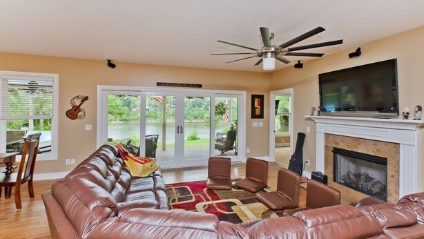 A living room with a leather sofa, a fireplace, a TV, and a ceiling fan. - Riverfront, Kayaks, Boat Dock, Games, Pool, Hot Tub, 10 Min To Dwntwn Nashville! (Nashville)