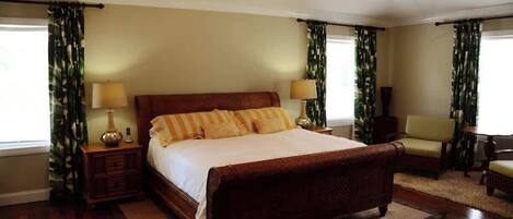 A bedroom with a large bed, two bedside tables with lamps, a ceiling fan, and a chair.