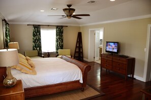 A bedroom with a large bed, a wooden dresser, a television, and a ceiling fan.