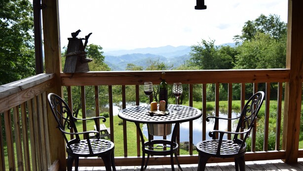 Eine Holzterrasse mit Tisch und zwei Stühlen mit Blick auf einen Fluss und Berge.