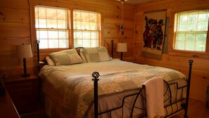 Ein Schlafzimmer einer Holzhütte mit einem Bett, zwei Nachttischen und einem Fenster mit Jalousien.