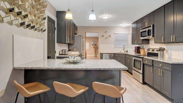 A modern kitchen with dark cabinets, a granite countertop, and three bar stools. - Close to Strip! Pool,  Spa,  Roulette Table,  Golf (Las Vegas)