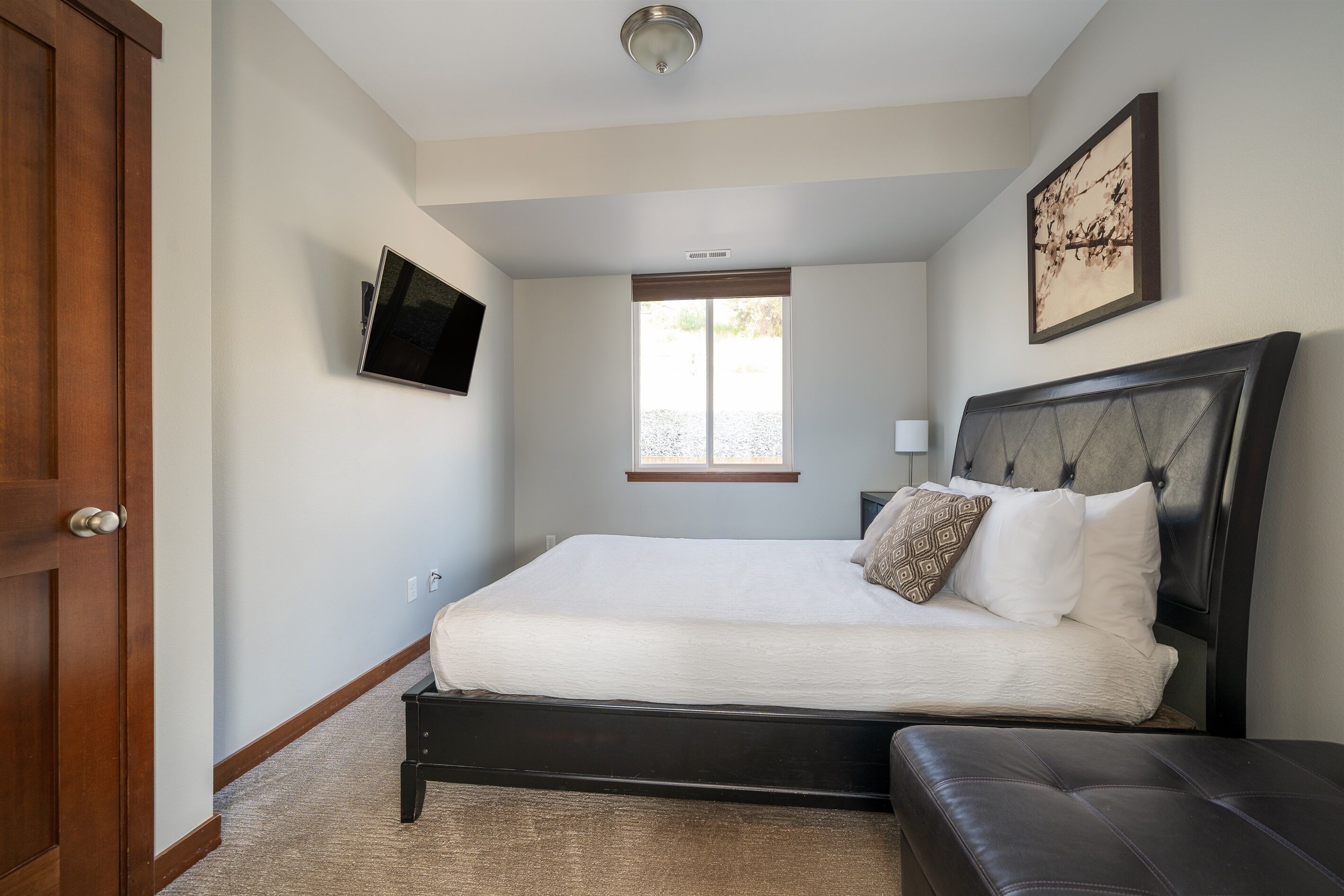 Une chambre à coucher avec un lit, un téléviseur fixé au mur, une fenêtre et une porte.