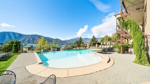 A pool area with lounge chairs, a clear view of mountains, and a building with a balcony.