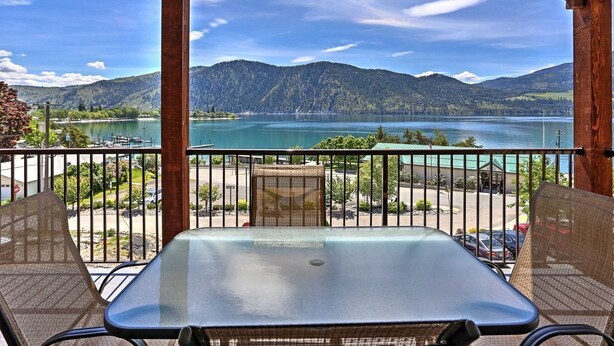 A balcony with a table and chairs, overlooking a lake and mountains.