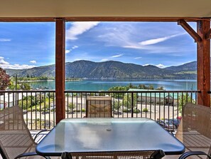 A balcony with a table and chairs, overlooking a lake and mountains.