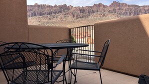 A balcony with a table and chairs, overlooking a desert landscape with rock formations. - 8A6 Amazing Views, Shared Pool/Hot Tub, Private Patio and Garage (MOAB)