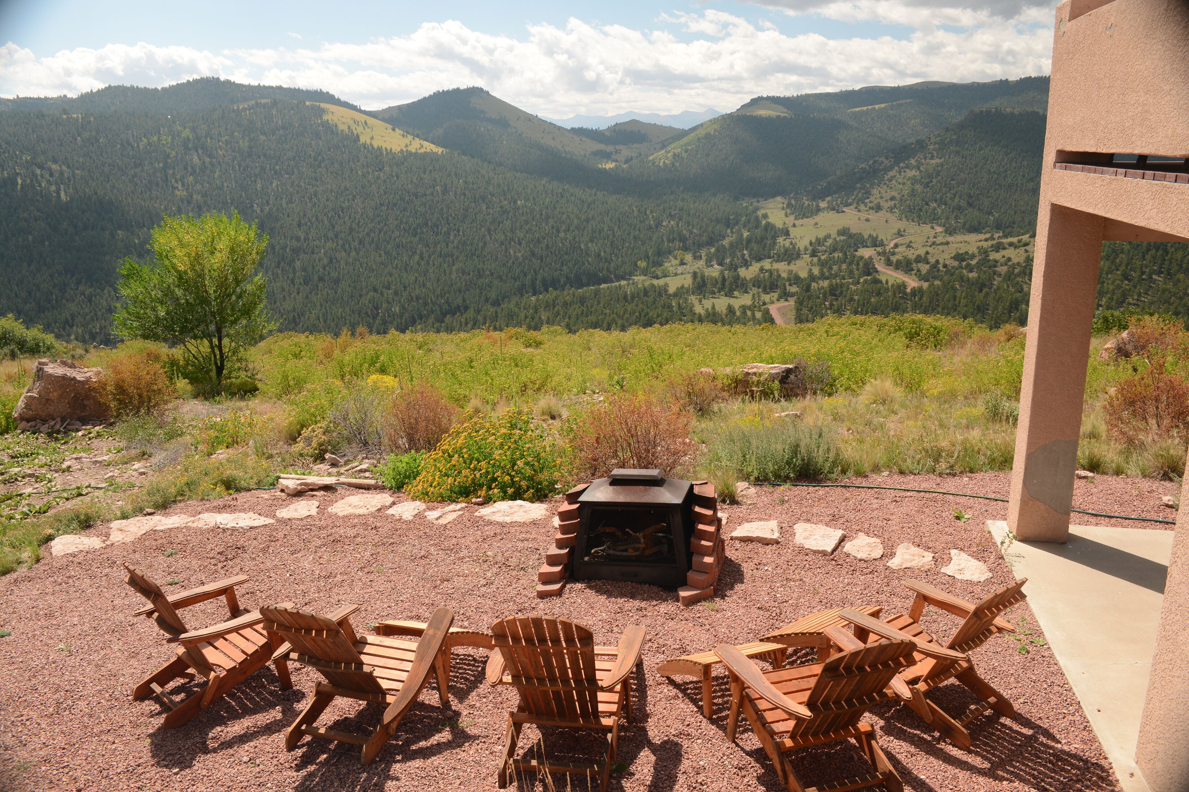A patio with wooden chairs and a fire pit, overlooking a mountainous landscape.