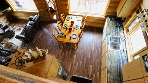 A wooden cabin interior with a dining area, a leather sofa, and a small kitchen. - Cpt Cook - Unique Alaskan log home in trees & wildflowers on 14-acre homestead. (Anchor Point)