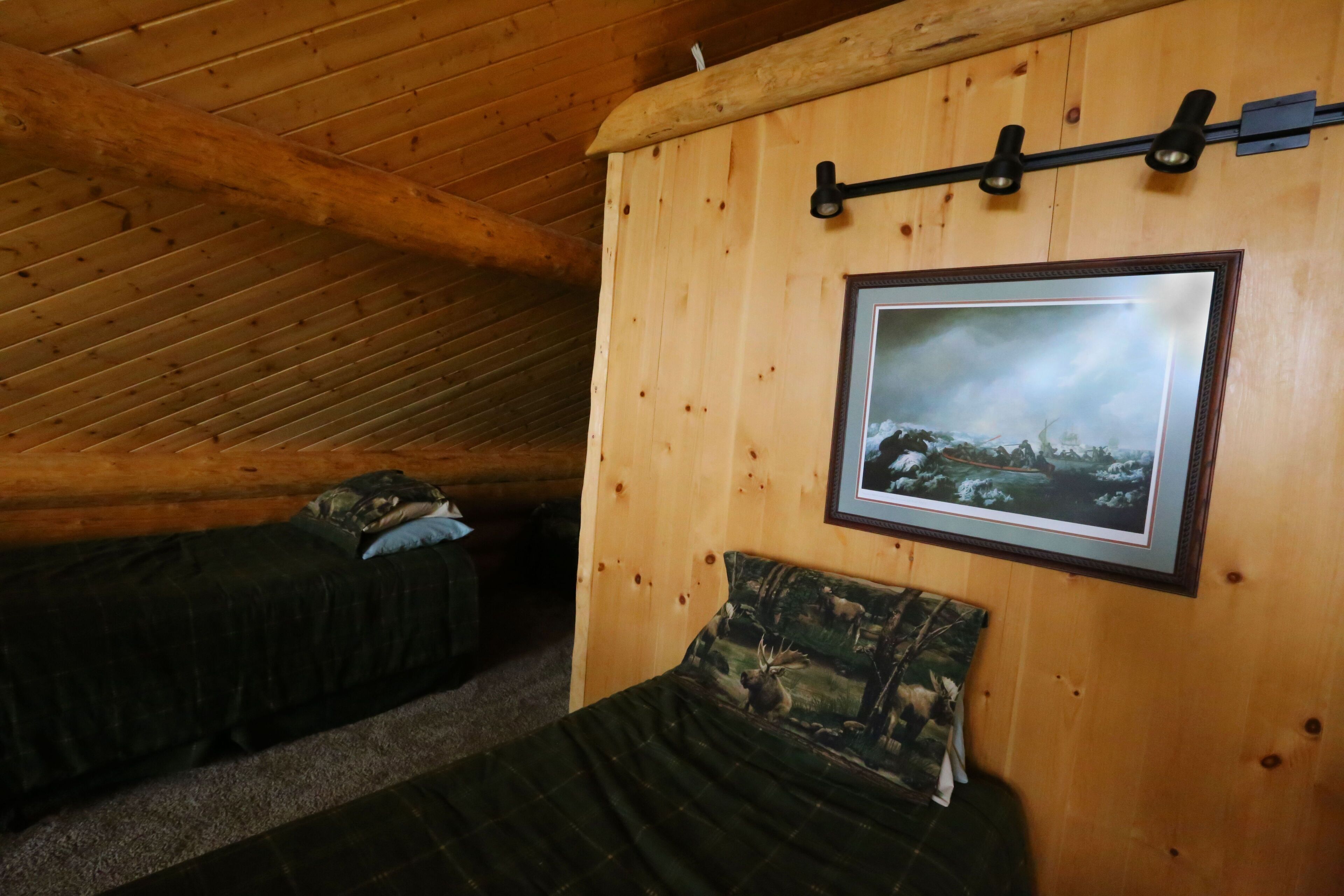 A cozy cabin room with wooden walls, a framed picture, and two beds with camouflage bedding.