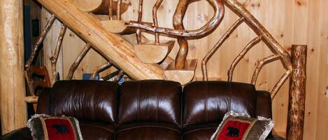 A brown leather sofa with two decorative pillows, a wooden staircase with a rustic design, and a wooden wall in the background.