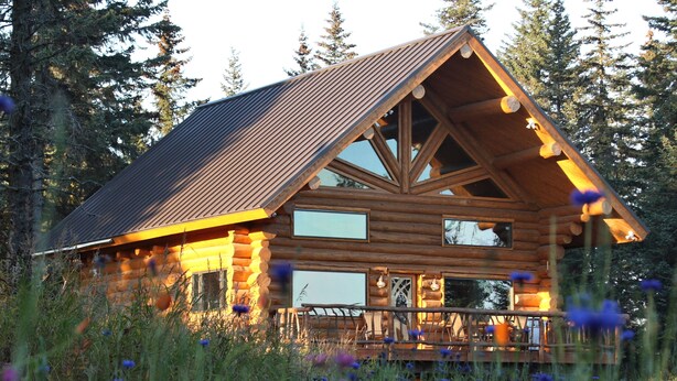 A log cabin with a large deck, surrounded by tall trees and wildflowers. - Cpt Cook - Unique Alaskan log home in trees & wildflowers on 14-acre homestead. (Anchor Point)