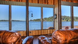 Una cabaña con amplios ventanales que dan a un lago, paredes de madera y asientos de cuero.